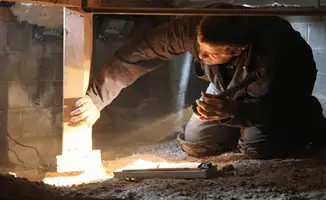 A professional inspecting wooden beams under the floor of a structure in Mobile, AL
