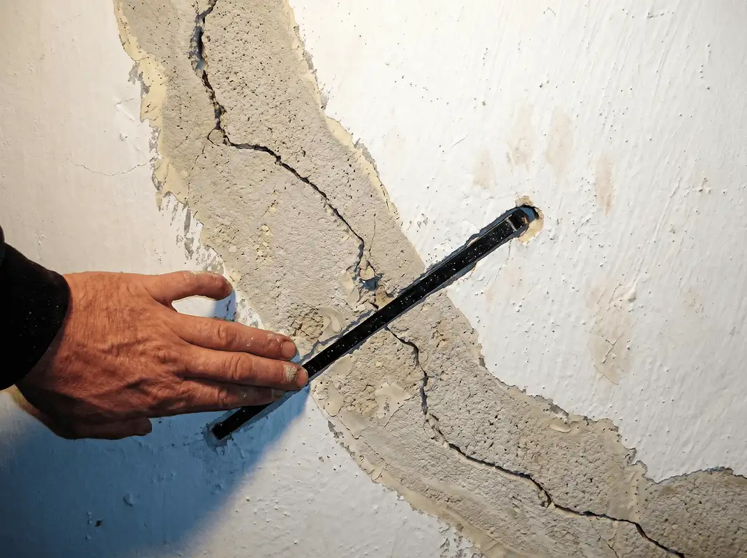 A wall with a large crack is being inspected by a professional in Mobile, AL